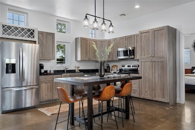Kitchen with concrete floors, appliances with stainless steel finishes, hanging light fixtures, a high ceiling, and brown cabinetry