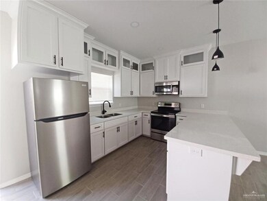 Kitchen with appliances with stainless steel finishes, a sink, a peninsula, white cabinets, and glass insert cabinets