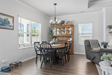 Dining area with crown molding, dark wood-style flooring, and a chandelier