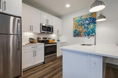 Kitchen featuring appliances with stainless steel finishes, white cabinets, backsplash, decorative light fixtures, and dark wood-type flooring