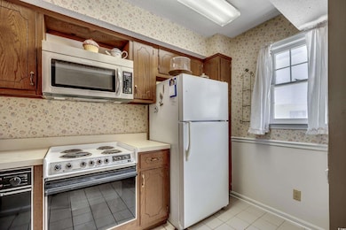 Kitchen with stainless steel microwave, freestanding refrigerator, range with electric cooktop, wallpapered walls, and light tile patterned flooring