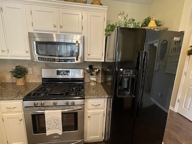 Kitchen with white cabinets, backsplash, dark stone counters, and appliances with stainless steel finishes