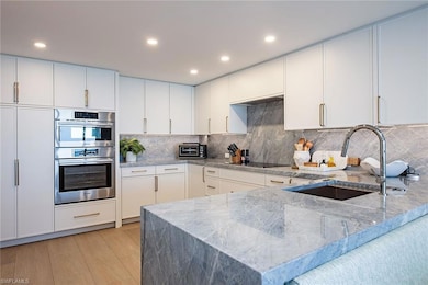 Kitchen featuring light stone countertops, white cabinets, tasteful backsplash, recessed lighting, and stainless steel double oven