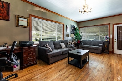 Living area with a chandelier, ornamental molding, light wood-style flooring, and a desk