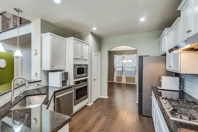 Kitchen with decorative backsplash, white cabinets, stainless steel appliances, pendant lighting, and dark stone counters