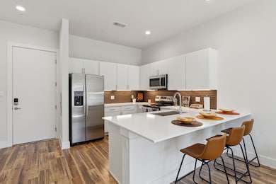 Kitchen with appliances with stainless steel finishes, a kitchen bar, a peninsula, white cabinetry, and dark wood-type flooring