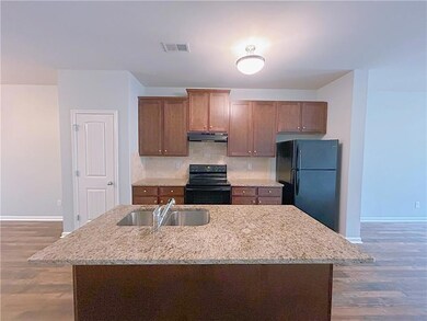 Kitchen featuring black appliances, under cabinet range hood, a sink, baseboards, and wood finished floors