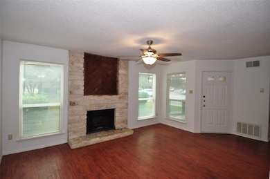 Unfurnished living room featuring dark wood-style flooring, a stone fireplace, a textured ceiling, and a ceiling fan