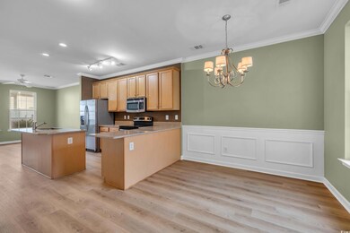 Kitchen featuring appliances with stainless steel finishes, ornamental molding, a chandelier, light wood-style floors, and a wainscoted wall