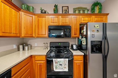 Kitchen featuring black appliances, brown cabinetry, and light stone countertops