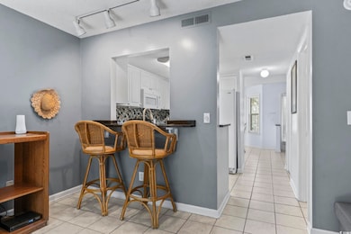 Kitchen with dark countertops, white cabinets, rail lighting, tasteful backsplash, and light tile patterned floors