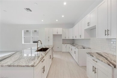 Kitchen with white cabinetry, light stone counters, tasteful backsplash, recessed lighting, and a center island with sink
