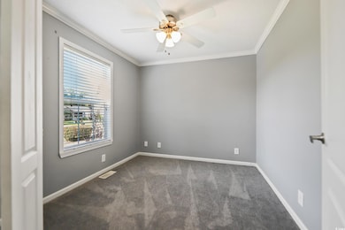 Spare room featuring dark carpet, a ceiling fan, ornamental molding, and baseboards