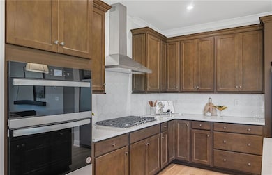 Kitchen with wall chimney range hood, stainless steel gas cooktop, light countertops, tasteful backsplash, and light wood finished floors