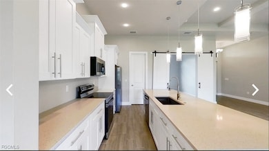 Kitchen featuring a barn door, white cabinets, stainless steel appliances, pendant lighting, and dark wood-style floors