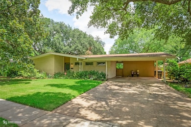 View of front facade featuring a front lawn, a carport, driveway, and brick siding