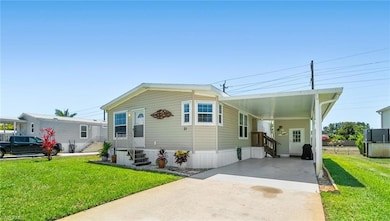 Manufactured / mobile home featuring entry steps, concrete driveway, an attached carport, and a front lawn