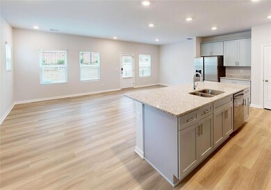 Kitchen featuring a sink, appliances with stainless steel finishes, gray cabinetry, light wood finished floors, and a center island with sink