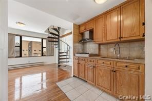 Kitchen featuring tasteful backsplash, brown cabinetry, light countertops, light wood-style flooring, and range hood