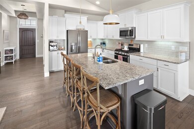 Kitchen featuring vaulted ceiling, stainless steel appliances, an island with sink, dark wood finished floors, and white cabinetry