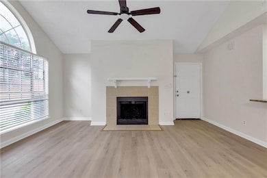 Unfurnished living room with vaulted ceiling, ceiling fan, wood finished floors, and a tiled fireplace