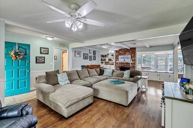 Living room with ceiling fan, a brick fireplace, wood-style floors, and built-in bookcase