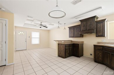 Kitchen with dark brown cabinets, hanging light fixtures, a peninsula, light tile patterned floors, and ceiling fan