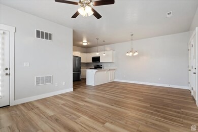 Unfurnished living room featuring light wood finished floors, ceiling fan, and a chandelier