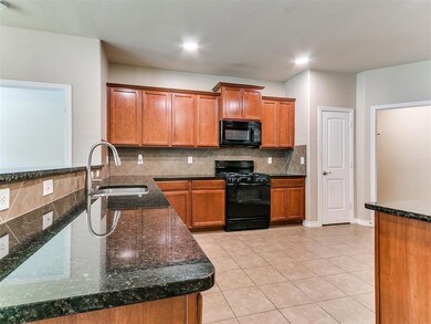 Kitchen featuring black appliances, a sink, brown cabinetry, decorative backsplash, and dark stone countertops