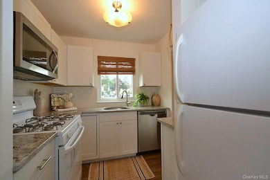 Kitchen featuring stainless steel appliances, white cabinets, backsplash, dark wood-style flooring, and light stone countertops