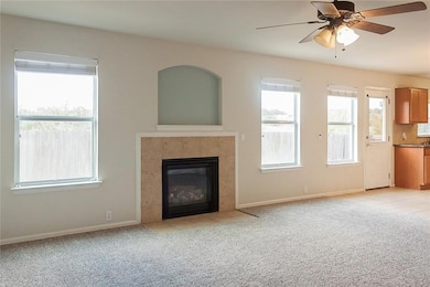 Unfurnished living room with a tiled fireplace, a ceiling fan, and light colored carpet