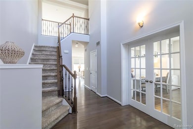 Staircase with healthy amount of natural light, wood finished floors, a towering ceiling, and french doors