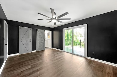 Unfurnished bedroom with access to exterior, a barn door, baseboards, and dark wood-style floors