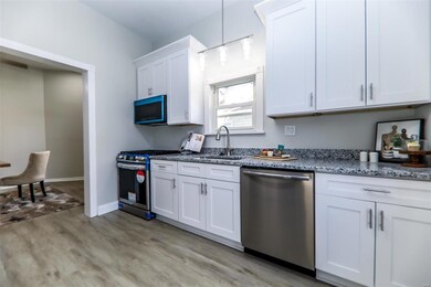 Kitchen featuring sink, light wood-type flooring, appliances with stainless steel finishes, decorative light fixtures, and white cabinetry