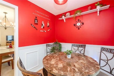 Dining space featuring a chandelier, a wainscoted wall, a decorative wall, and carpet flooring