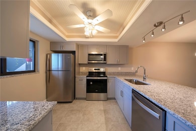 Kitchen featuring stainless steel appliances, light stone counters, a raised ceiling, and gray cabinets