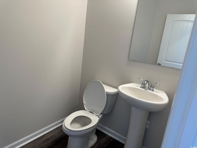 Half bath with baseboards, a sink, toilet, and wood finished floors
