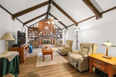 Living room with beam ceiling, wood finished floors, a fireplace, and high vaulted ceiling