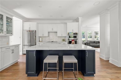 Kitchen featuring stainless steel appliances, tasteful backsplash, white cabinetry, a large island, and crown molding