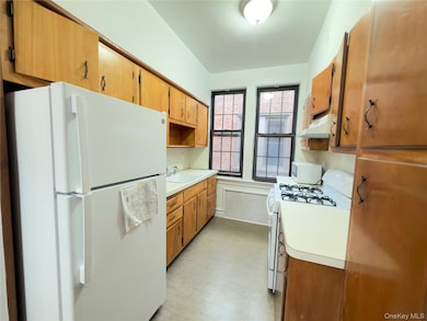 Kitchen featuring white appliances, light countertops, under cabinet range hood, and brown cabinets