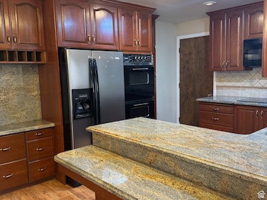 Kitchen featuring tasteful backsplash, light stone countertops, recessed lighting, light wood-type flooring, and black appliances
