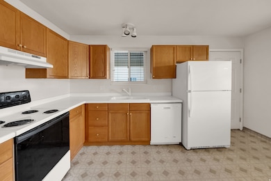 Kitchen featuring white appliances, light floors, light countertops, under cabinet range hood, and brown cabinetry