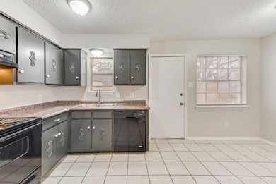 Kitchen featuring black appliances, dark countertops, a textured ceiling, plenty of natural light, and light tile patterned floors