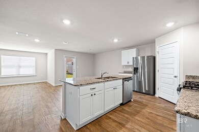 Kitchen featuring an island with sink, sink, white cabinetry, stainless steel appliances, and light wood-type flooring