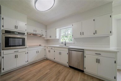 Kitchen with appliances with stainless steel finishes, light wood-style floors, white cabinetry, a sink, and light countertops