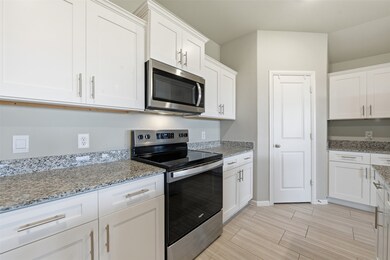 Kitchen featuring appliances with stainless steel finishes, white cabinets, wood finish floors, and light stone counters