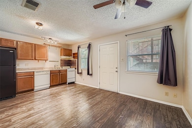 Kitchen featuring white appliances, a textured ceiling, light countertops, brown cabinets, and light wood-style flooring