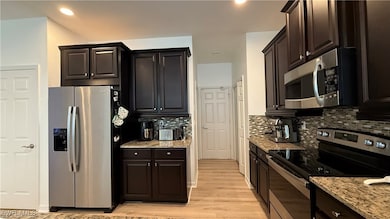 Kitchen featuring stainless steel appliances, light wood-style floors, backsplash, light stone counters, and recessed lighting