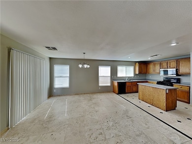 Kitchen featuring brown cabinets, a textured ceiling, black appliances, a chandelier, and light countertops
