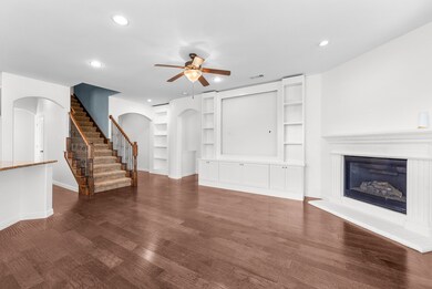 Unfurnished living room featuring built in features, stairs, dark wood finished floors, a ceiling fan, and a glass covered fireplace
